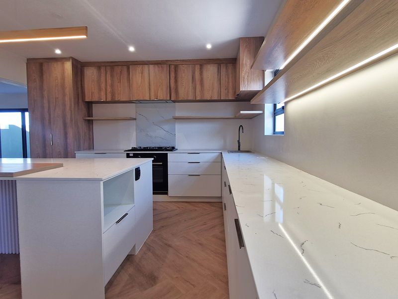 Modern kitchen featuring high-end cabinetry, stone countertops, a central island, integrated appliances, and stylish herringbone flooring with ambient LED lighting.