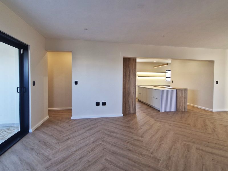 Spacious open-plan living area featuring modern herringbone flooring, recessed lighting, and a sleek kitchen island, seamlessly connecting to an outdoor patio.