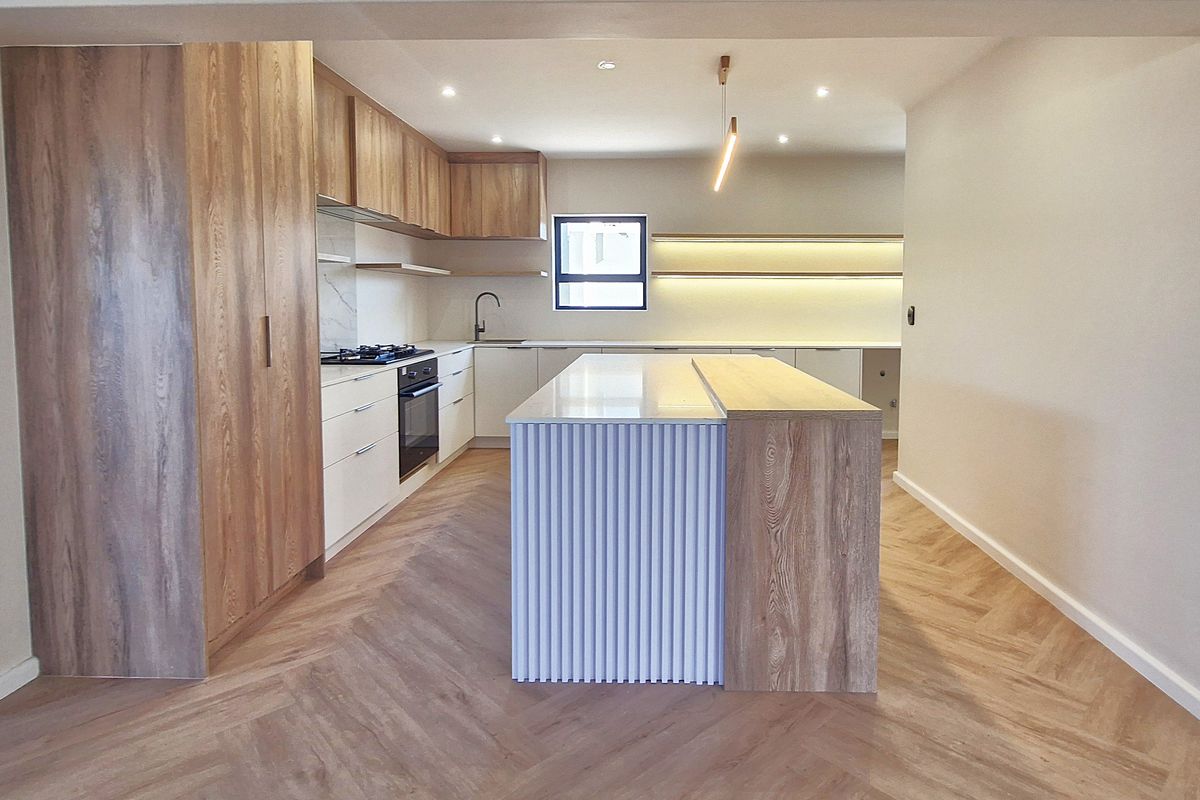 Modern kitchen featuring a large island with fluted detailing, wood-grain cabinetry, stone countertops, herringbone flooring, and integrated appliances.