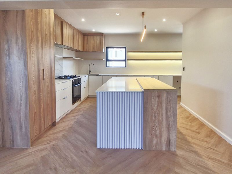 Modern kitchen featuring a large island with fluted detailing, wood-grain cabinetry, stone countertops, herringbone flooring, and integrated appliances.