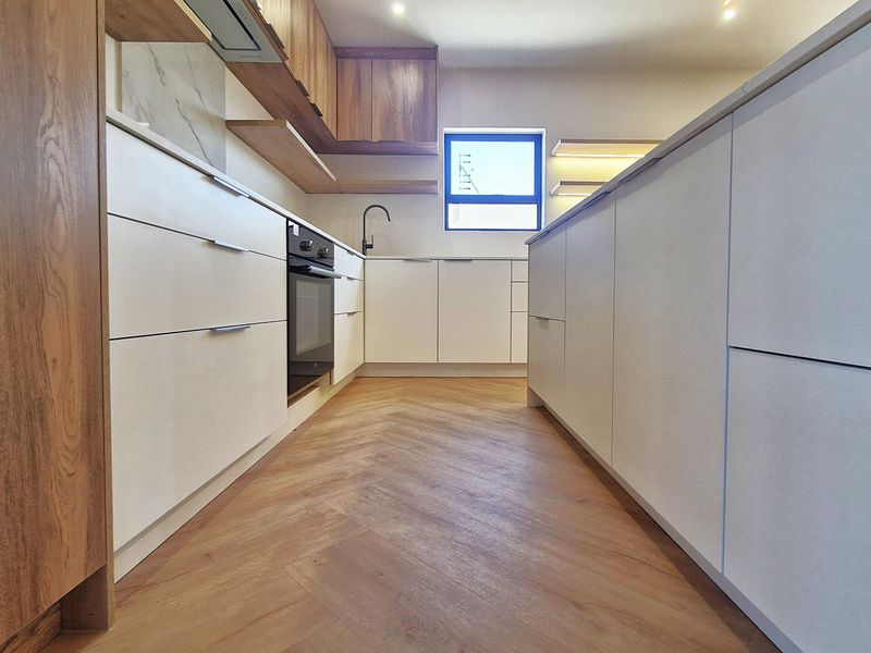 Modern kitchen featuring sleek white cabinetry, wood-tone accents, integrated oven, and stylish herringbone flooring in a clean, contemporary design.