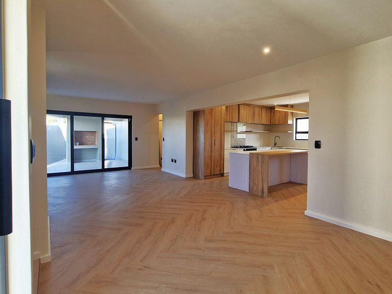 Spacious open-plan living area featuring modern herringbone flooring, a contemporary kitchen with island, and seamless flow to an outdoor patio with built-in braai.