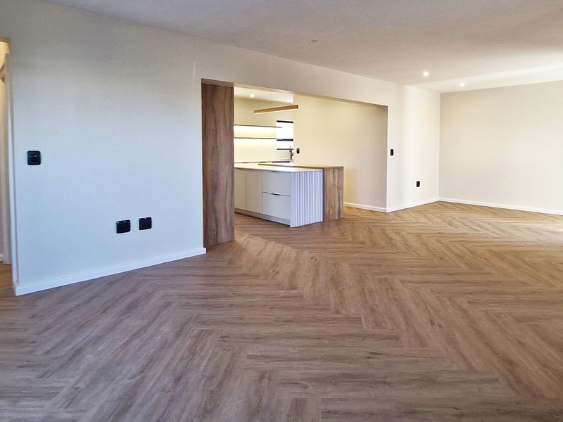 Spacious open-plan living area featuring modern herringbone flooring, recessed lighting, and a sleek, contemporary kitchen with a central island.
