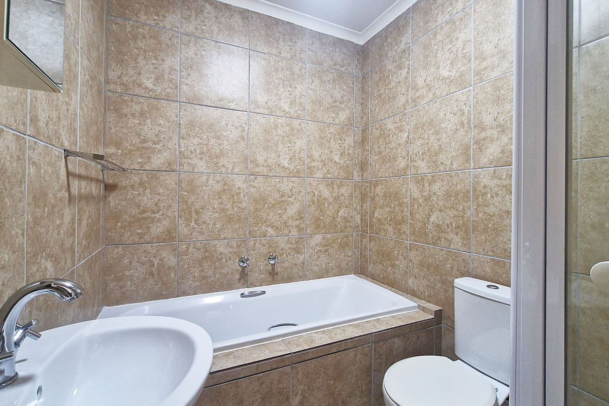 A functional bathroom featuring a built-in bathtub, pedestal basin, and toilet, finished with neutral ceramic wall tiling.