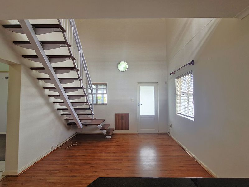 Spacious living area featuring high ceilings, laminate flooring, and an open-tread staircase leading to the upper level.