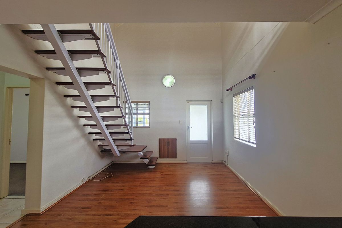 Spacious living area featuring high ceilings, laminate flooring, and an open-tread staircase leading to the upper level.