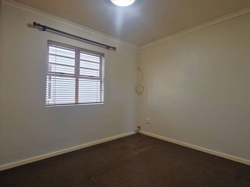 An empty bedroom featuring carpet flooring, a built-in wardrobe, and a window with fitted blinds.