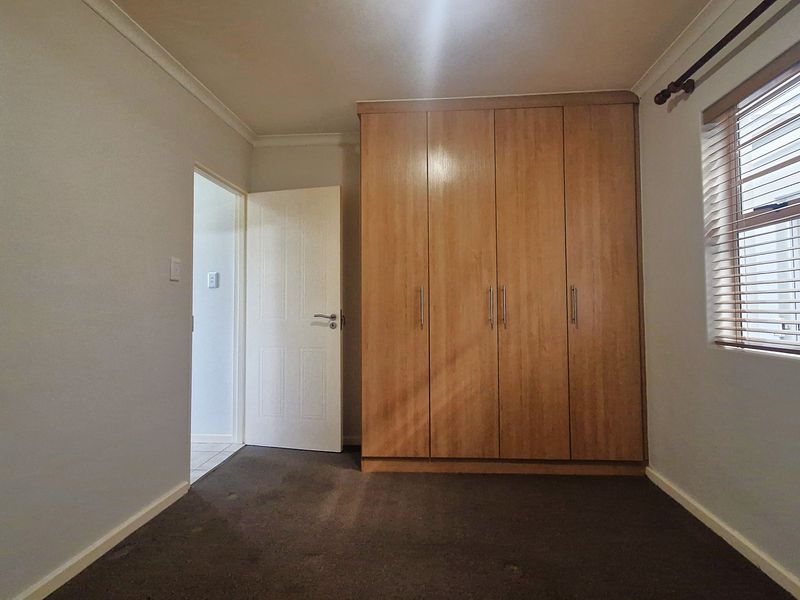 A clean, empty bedroom featuring built-in wooden wardrobes, carpeted flooring, and venetian blinds on the window.