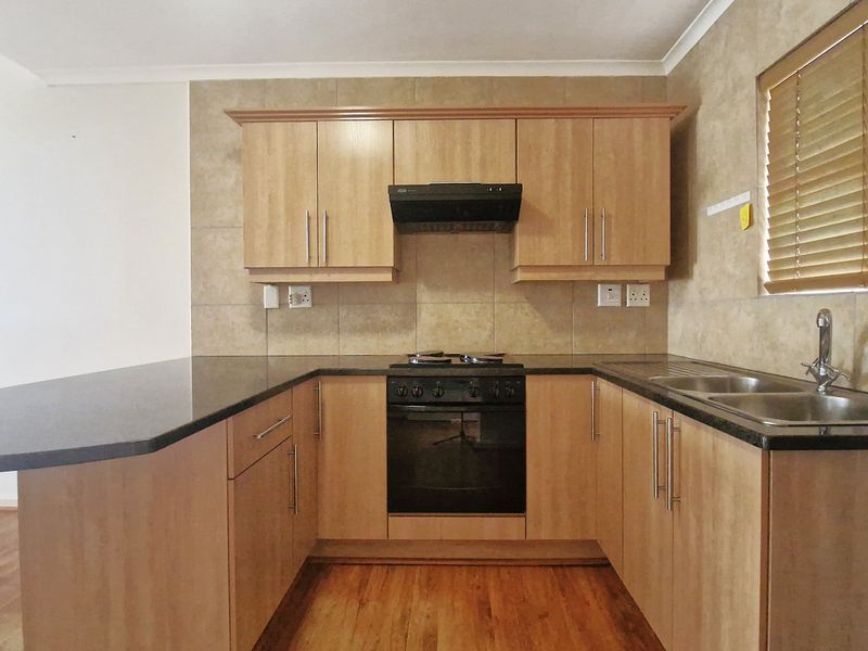 A functional kitchen featuring light wood cabinetry, dark laminate countertops, a built-in oven with hob, and a double sink with tiled backsplash.