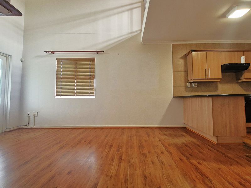 Open-plan living area featuring laminate flooring, a staircase, and a functional kitchen with built-in cabinetry and integrated appliances.