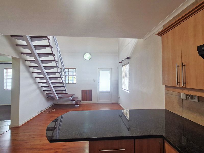 Open plan kitchen and living area featuring a modern staircase, granite countertops, and laminate flooring in a bright, spacious layout.