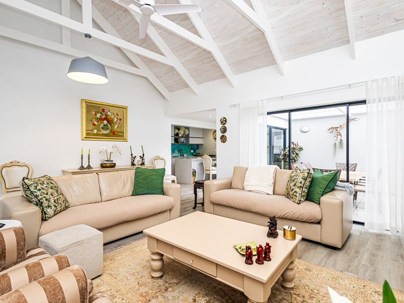 Spacious open-plan living area featuring a high vaulted ceiling with exposed beams, ceiling fan, and large sliding doors leading to an outdoor patio.