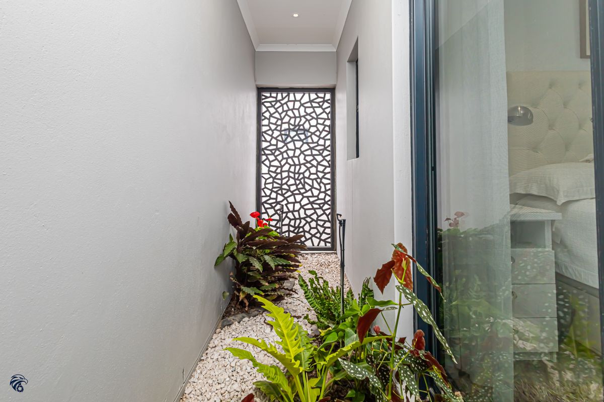 A narrow, well-maintained side passage featuring a decorative metal privacy screen, pebble landscaping, and recessed lighting.