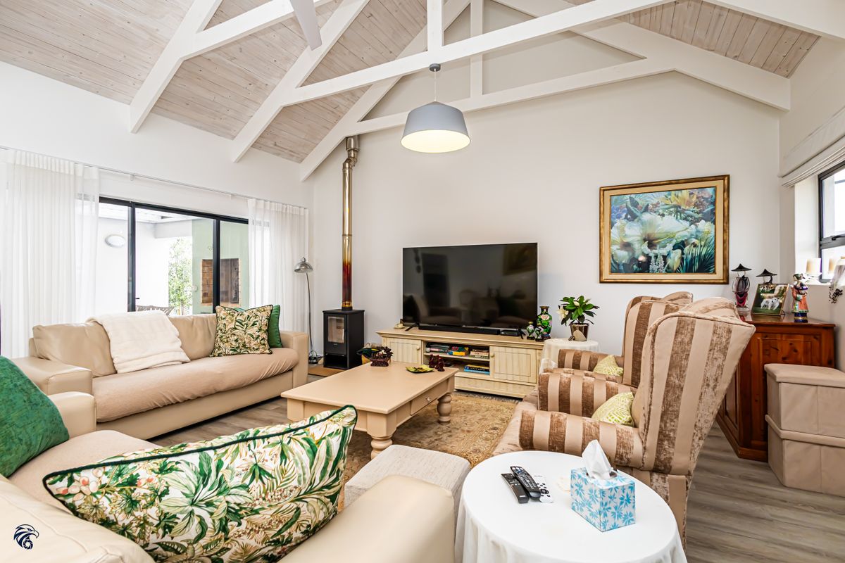 Spacious living room featuring a high vaulted ceiling with exposed beams, a wood-burning fireplace, and large sliding glass doors leading to the patio.