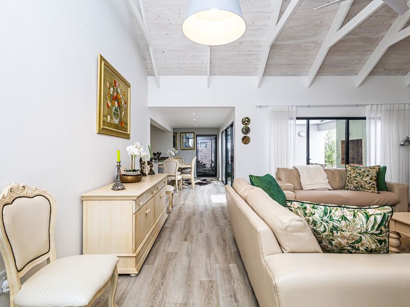 Spacious open-plan living area featuring vaulted ceilings with exposed rafters, modern laminate flooring, and large sliding glass doors leading to the exterior.