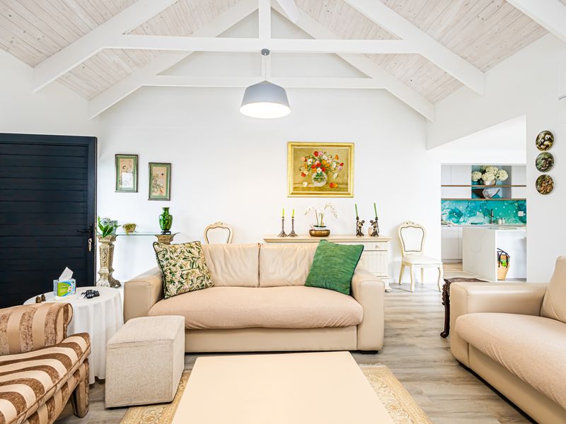 Spacious open-plan living area featuring a high vaulted ceiling with exposed beams, flowing seamlessly into a modern kitchen with stone countertops.