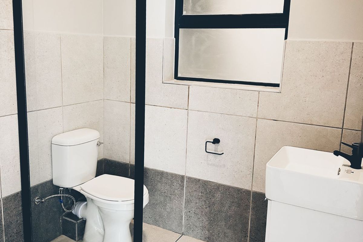 Modern bathroom featuring a wall-mounted vanity, black tapware, a glass shower screen, and neutral floor-to-ceiling tiling with a frosted window.