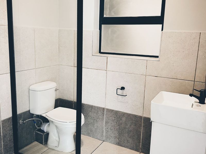 Modern bathroom featuring a wall-mounted vanity, black tapware, a glass shower screen, and neutral floor-to-ceiling tiling with a frosted window.