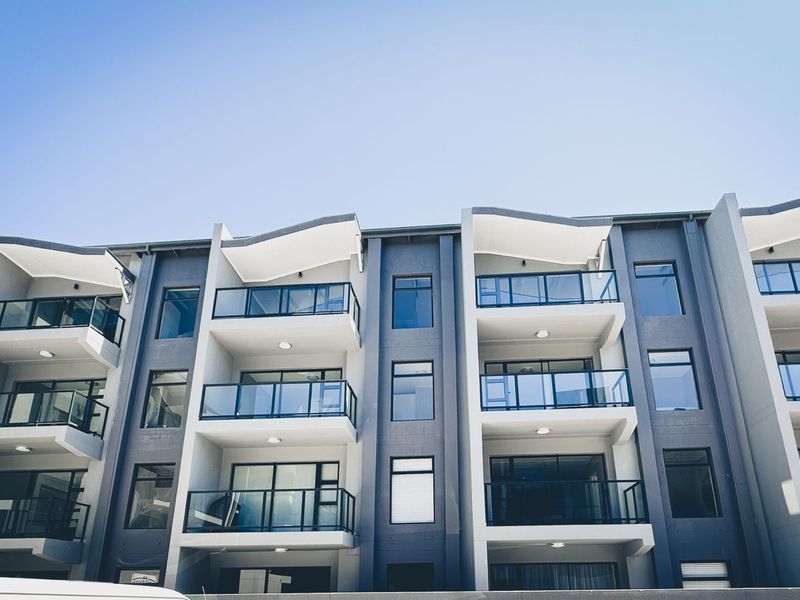 A modern apartment building facade featuring multiple levels with private balconies, glass balustrades, and contemporary architectural design.