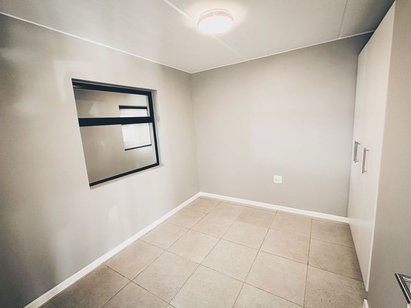 A clean, empty bedroom featuring neutral grey walls, tiled flooring, and a built-in wardrobe, offering a versatile space ready for personalization.