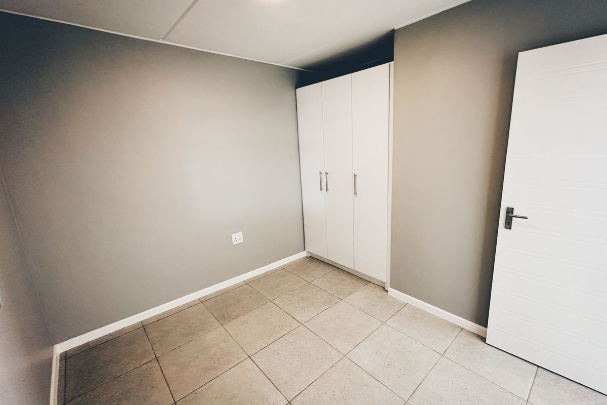 A clean, empty bedroom featuring neutral grey walls, tiled flooring, and a built-in white wardrobe.