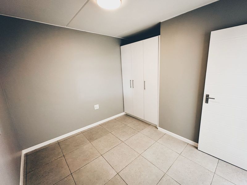 A clean, empty bedroom featuring neutral grey walls, tiled flooring, and a built-in white wardrobe.