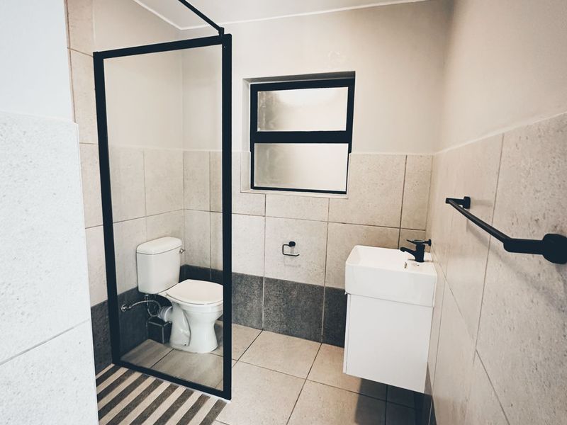 Modern bathroom featuring a walk-in shower with a black-framed glass screen, wall-mounted vanity, and neutral tiled finishes throughout.