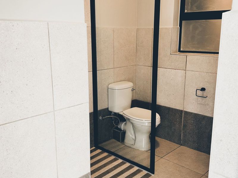 A modern bathroom featuring neutral-toned wall and floor tiles, a sleek black-framed glass shower screen, and a standard toilet.