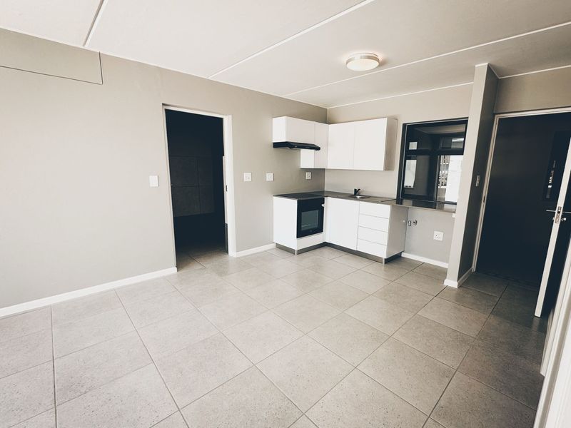 An open-plan living and kitchen area featuring neutral tiled flooring, modern white cabinetry, and integrated cooking appliances.