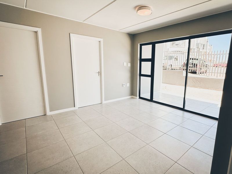 A bright, empty living area featuring neutral tiled flooring, modern internal doors, and a large sliding glass door providing access to the exterior.