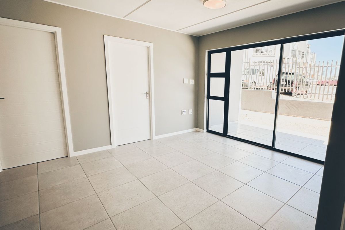 A bright, empty living area featuring neutral tiled flooring, modern internal doors, and a large sliding glass door providing access to the exterior.