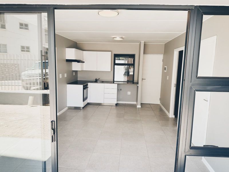 Modern open-plan kitchen and living area featuring neutral tones, tiled flooring, and direct access to the exterior through a sliding glass door.