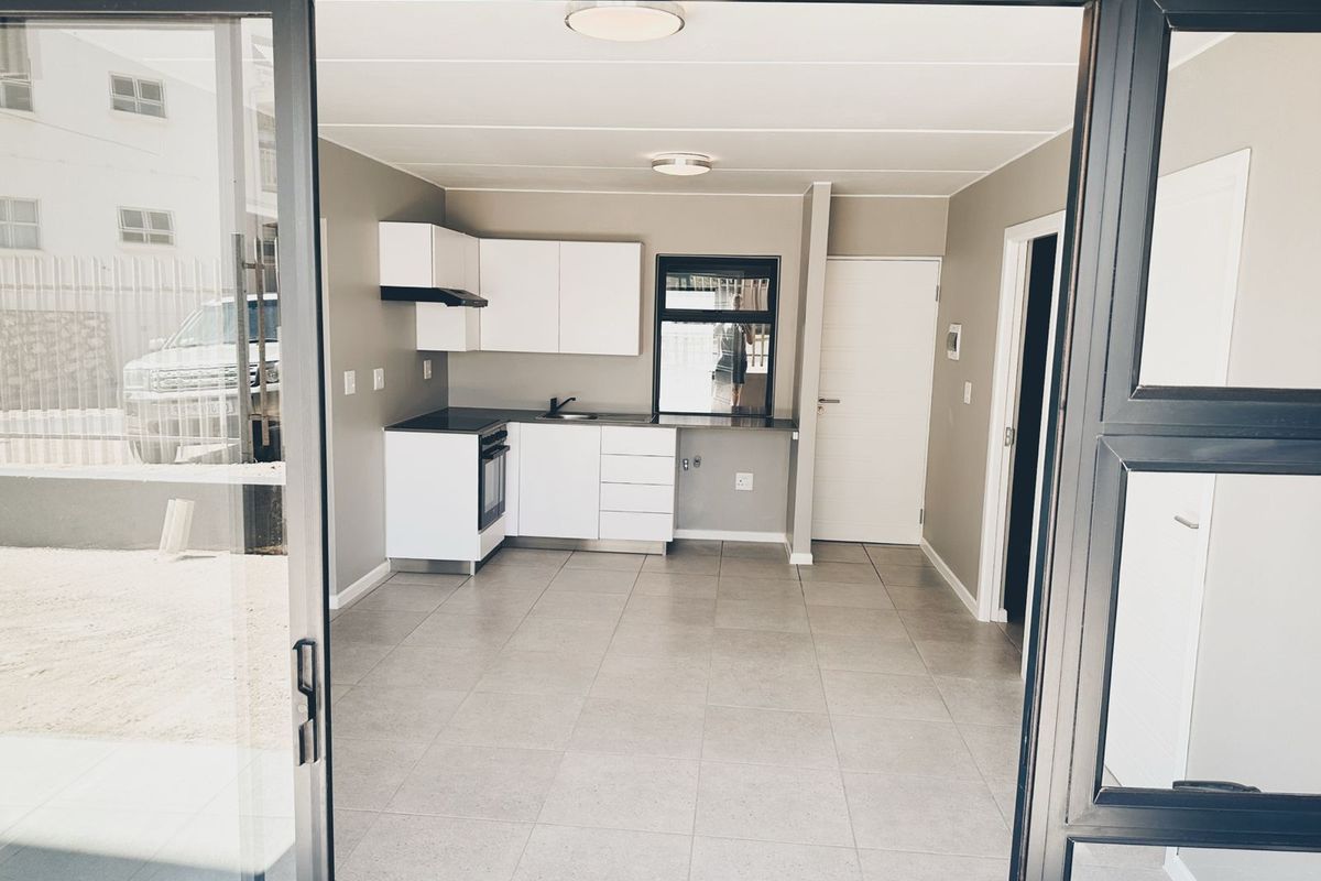Modern open-plan kitchen and living area featuring neutral tones, tiled flooring, and direct access to the exterior through a sliding glass door.