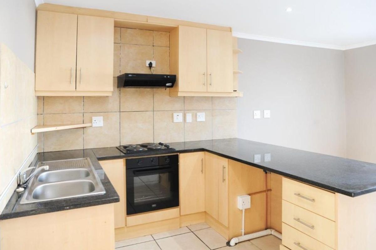 A functional kitchen featuring light wood cabinetry, dark laminate countertops, built-in oven, gas hob, and tiled backsplash with an open-plan layout.
