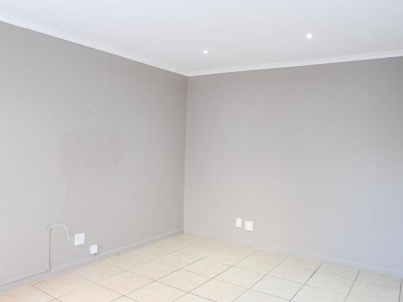 A vacant living area featuring neutral grey walls, tiled flooring, and recessed downlighting, providing a clean canvas for interior design.