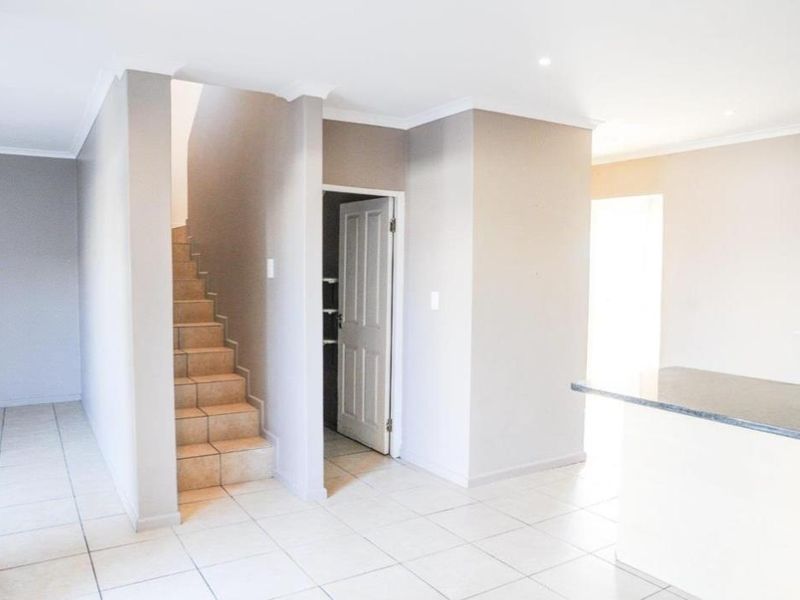 Open plan living area featuring tiled flooring, a staircase, and a kitchen counter, providing a bright and neutral blank canvas for interior design.