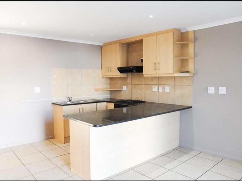 A clean, functional kitchen featuring light wood cabinetry, dark granite countertops, a gas hob with extractor, and neutral tiled flooring.
