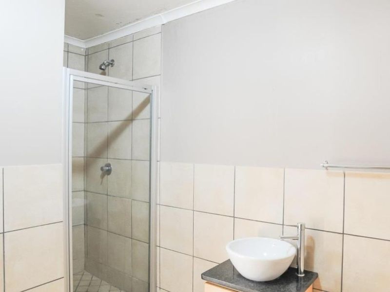 A functional bathroom featuring a glass-enclosed shower, a modern vessel sink on a vanity countertop, and neutral wall tiling.