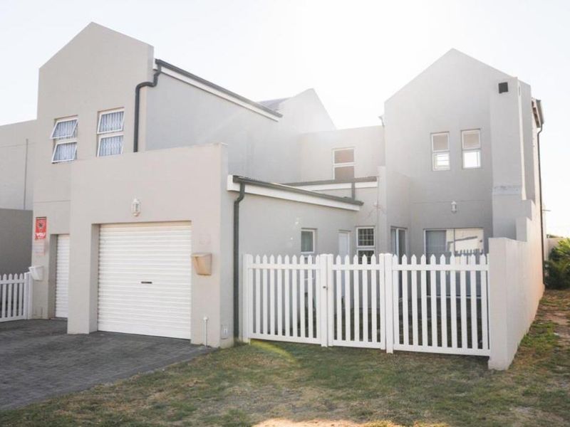 Front elevation of a modern double-story townhouse featuring a single garage, paved driveway, and white picket fencing.