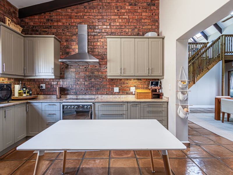 A well-appointed kitchen featuring exposed brick walls, shaker-style cabinetry, stone countertops, and terracotta flooring, with an open-plan layout leading to the dining area.