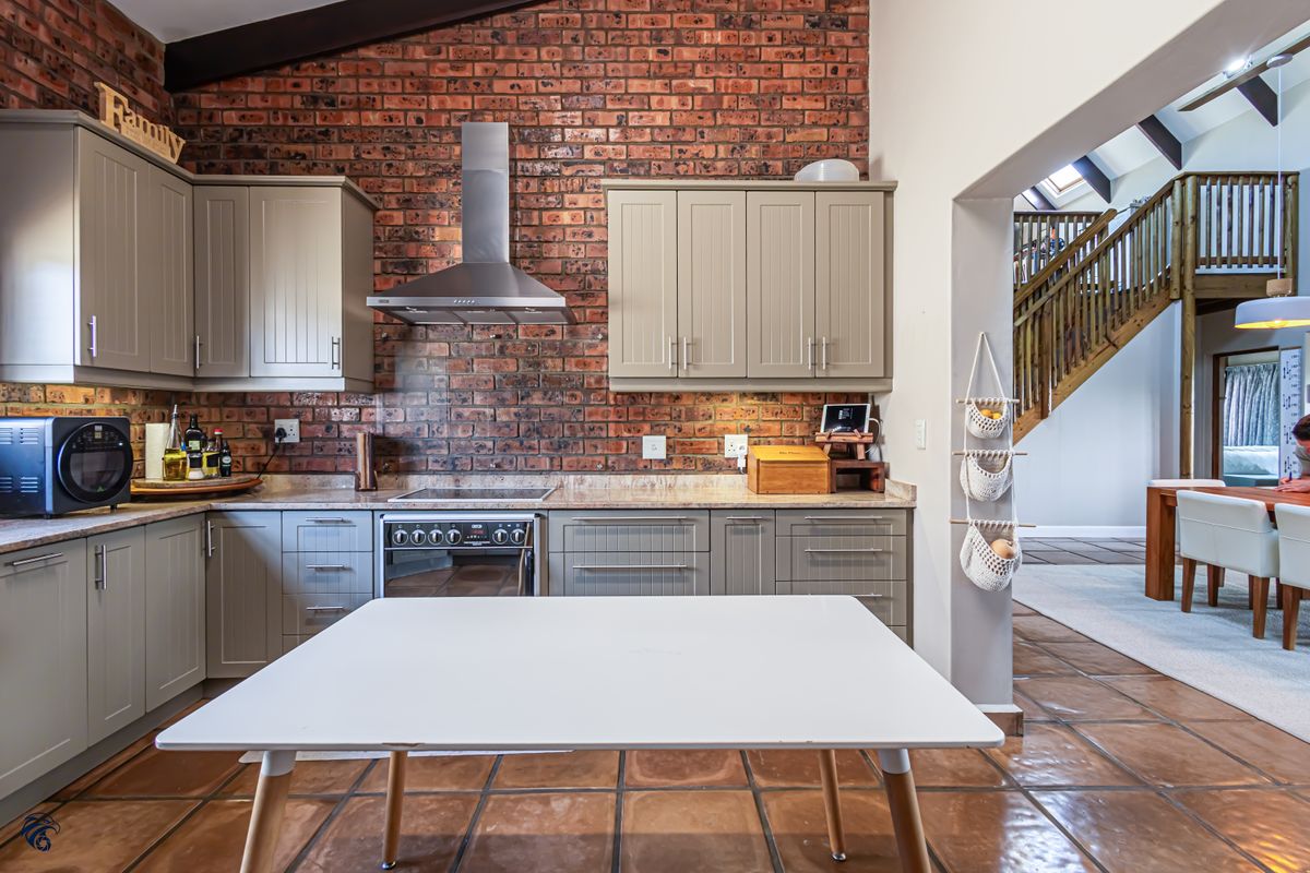 A well-appointed kitchen featuring exposed brick walls, shaker-style cabinetry, stone countertops, and terracotta flooring, with an open-plan layout leading to the dining area.