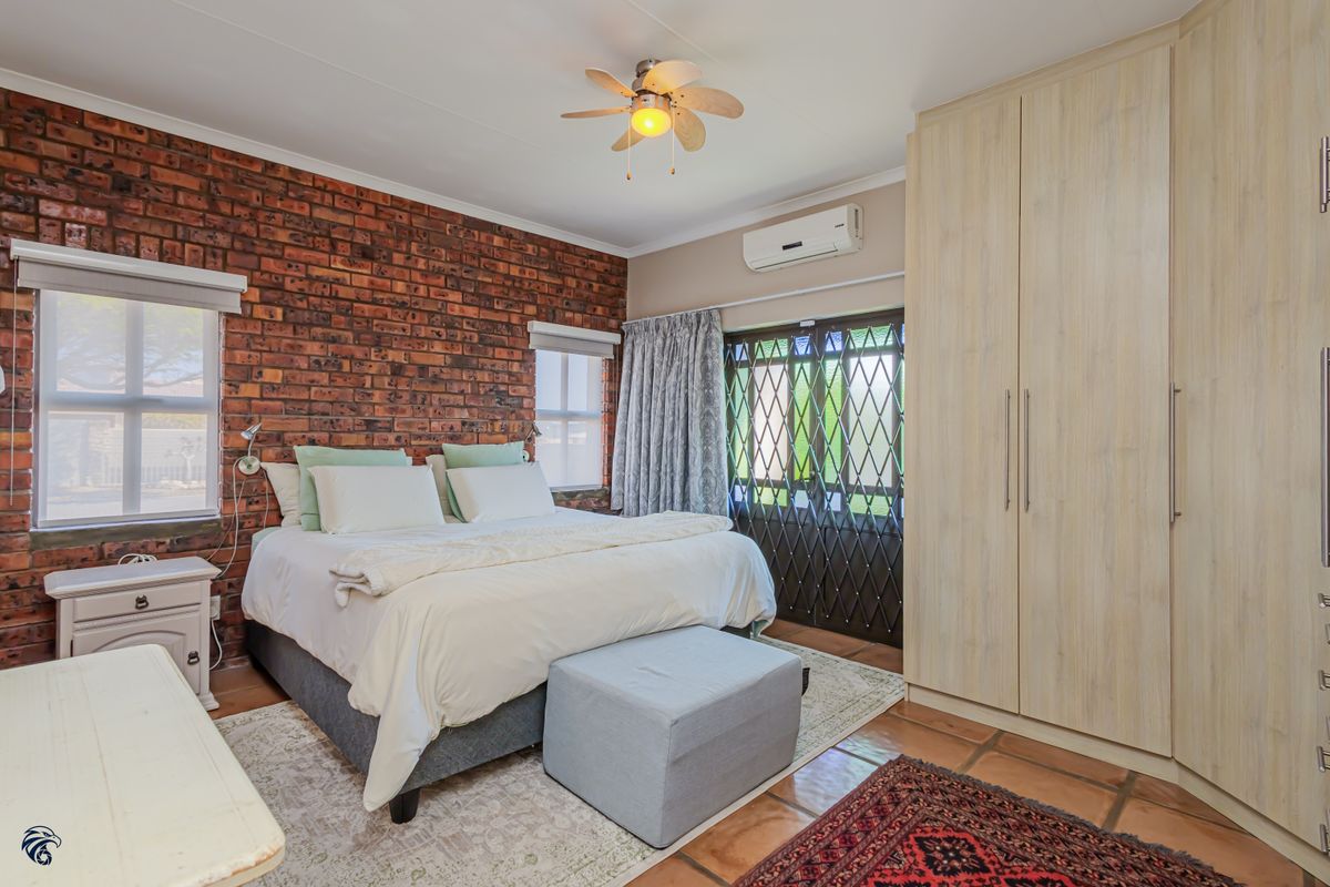 Spacious bedroom featuring an exposed brick wall, built-in cupboards, ceiling fan, air conditioning, and direct access to the exterior via a security gate.