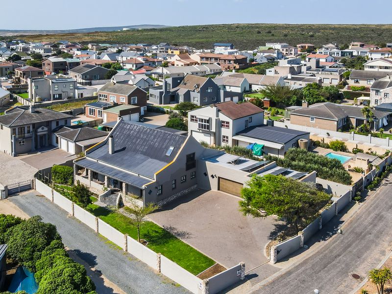 Aerial view of the property showcasing the main dwelling, paved driveway, garage, and surrounding residential neighborhood.