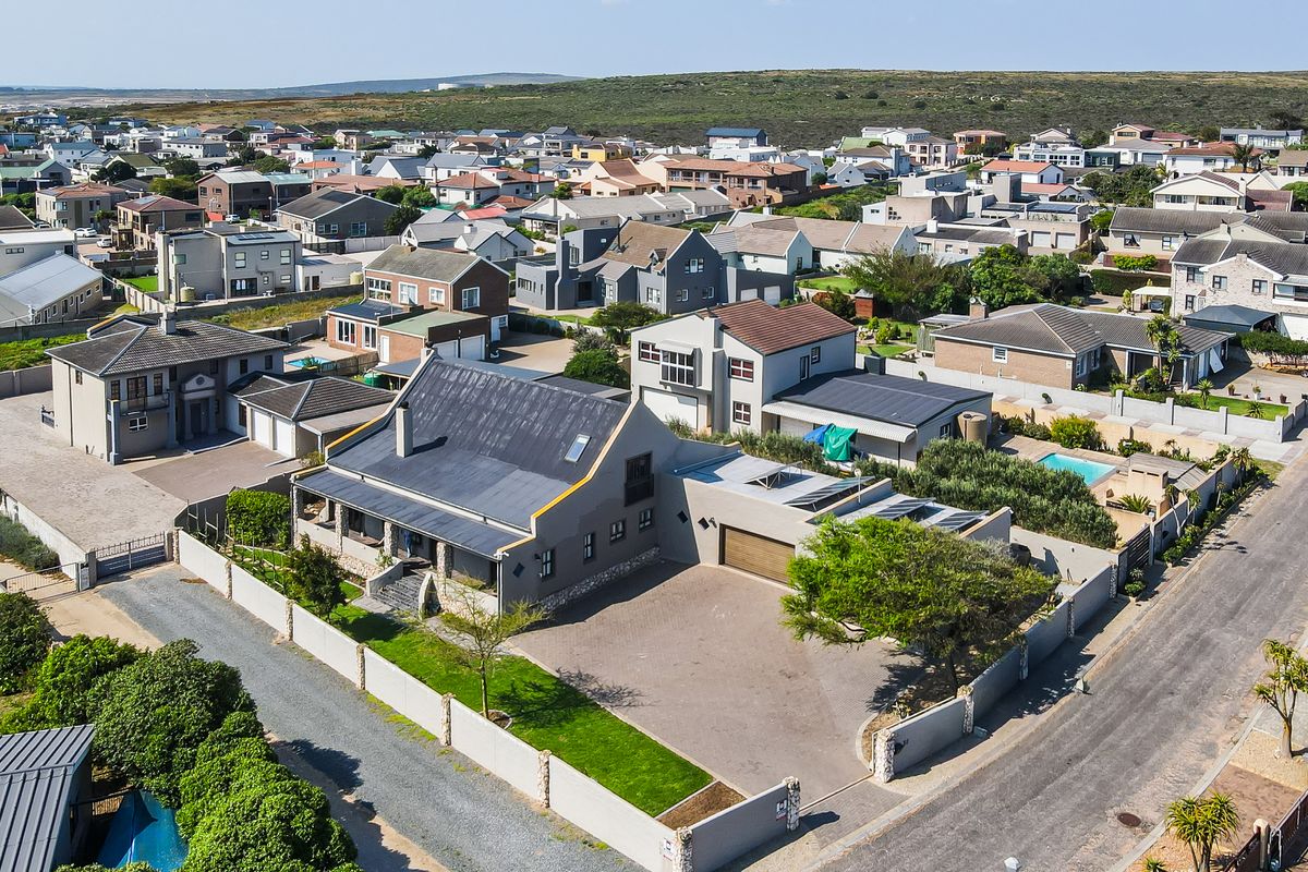 Aerial view of the property showcasing the main dwelling, paved driveway, garage, and surrounding residential neighborhood.