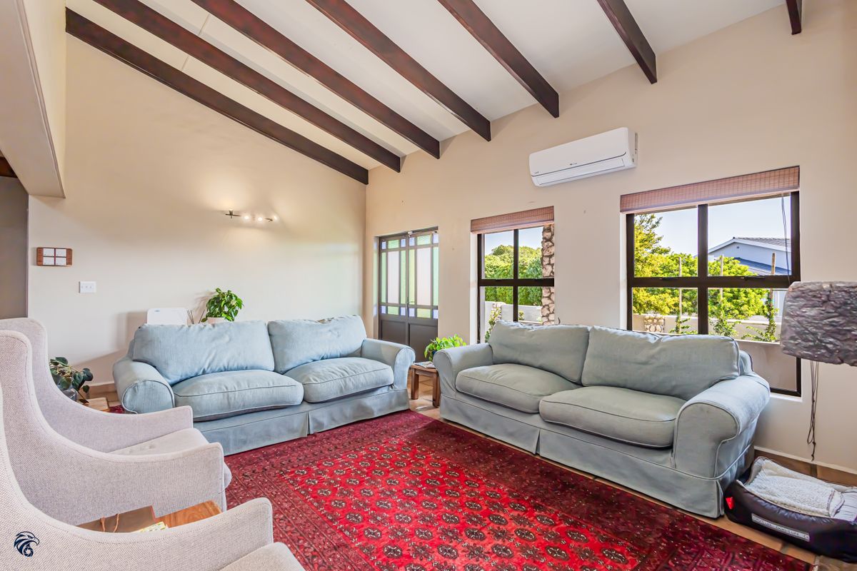 Spacious living room featuring high vaulted ceilings with exposed timber beams, large windows for natural light, and a wall-mounted air conditioning unit.