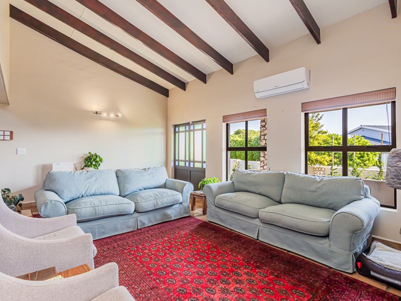 Spacious living room featuring high vaulted ceilings with exposed timber beams, large windows for natural light, and a wall-mounted air conditioning unit.