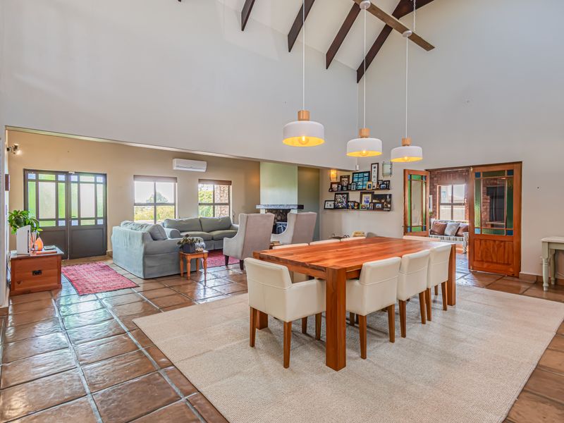 Spacious open-plan living and dining area featuring high vaulted ceilings with exposed timber beams, terracotta flooring, and a cozy fireplace.