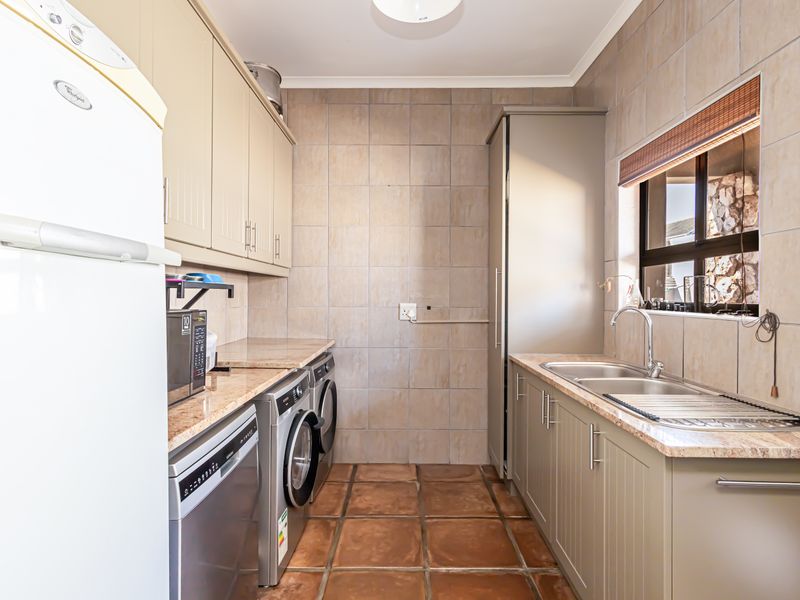 A functional laundry room featuring built-in cabinetry, laminate countertops, a double basin sink, and tiled finishes throughout.