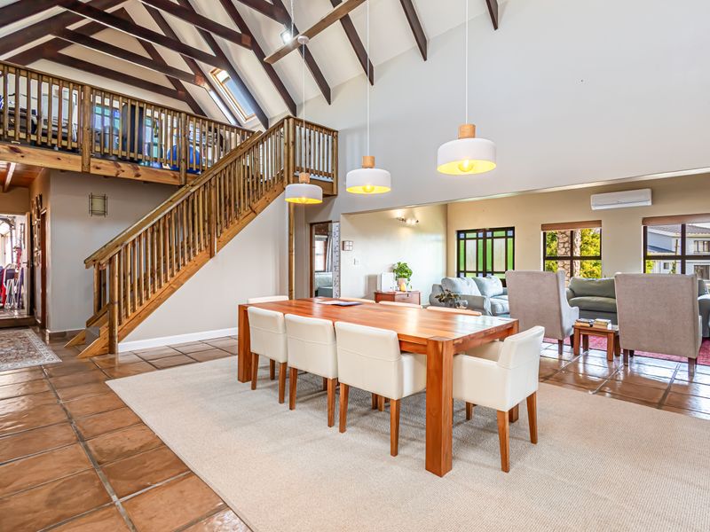 Spacious open-plan living and dining area featuring high vaulted ceilings with exposed timber trusses, a mezzanine level, and classic terracotta floor tiles.
