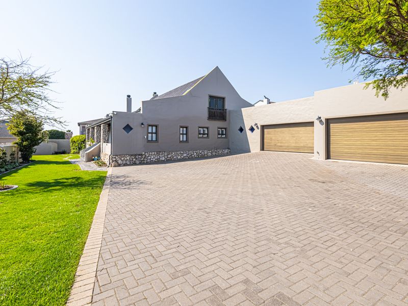 Front exterior view of the property featuring a paved driveway, double garage, stone-clad base, and a small balcony.